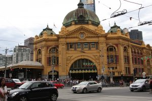 in front of the Flinders Street Train Station with cars and a few Christmas decorations