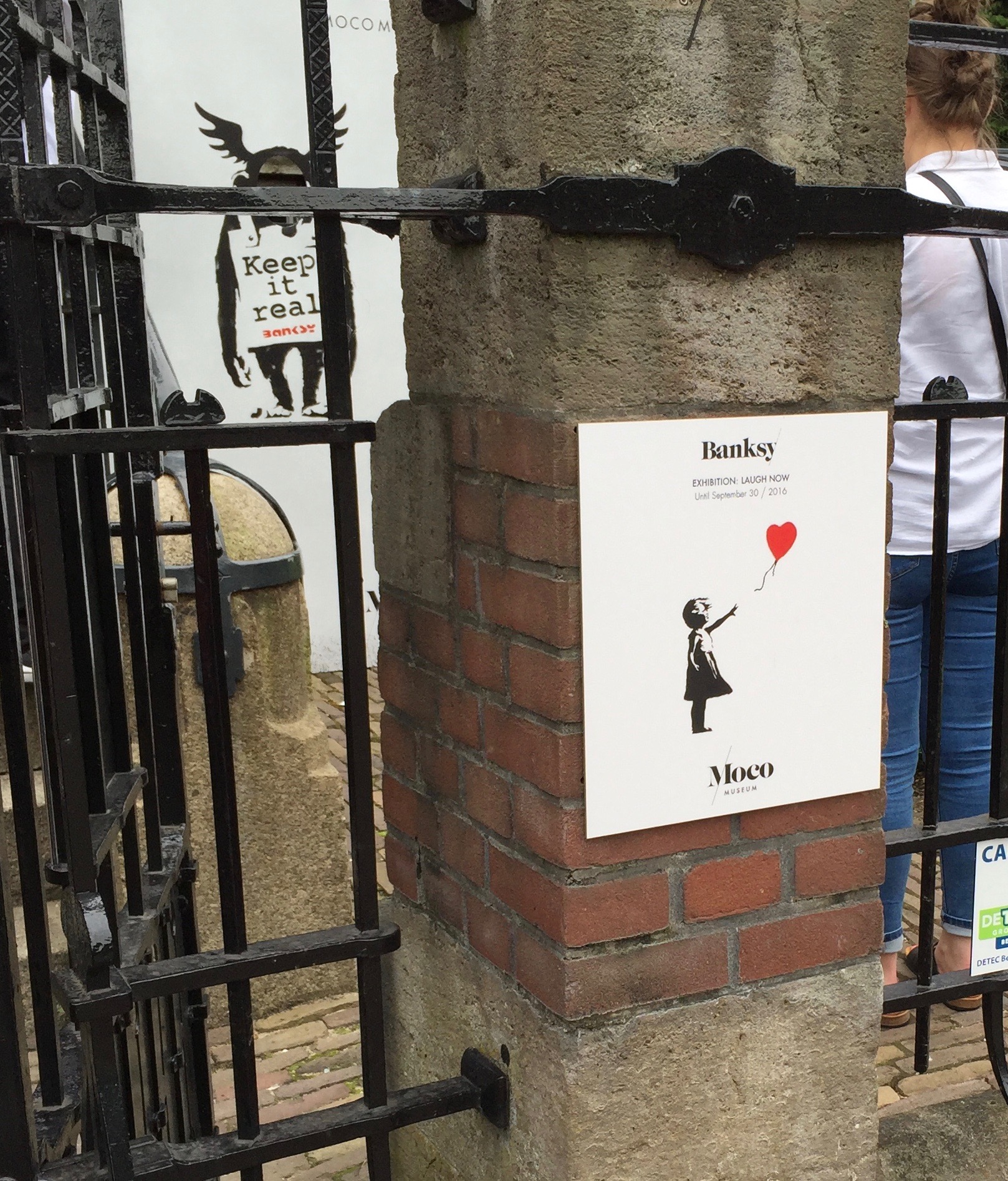 Moco Museum Banksy little girl with a heart balloon sign on the fence post outside of the museum in Amsterdam